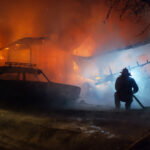 Firefighter putting with the hose out the fire of the house and car at night accident